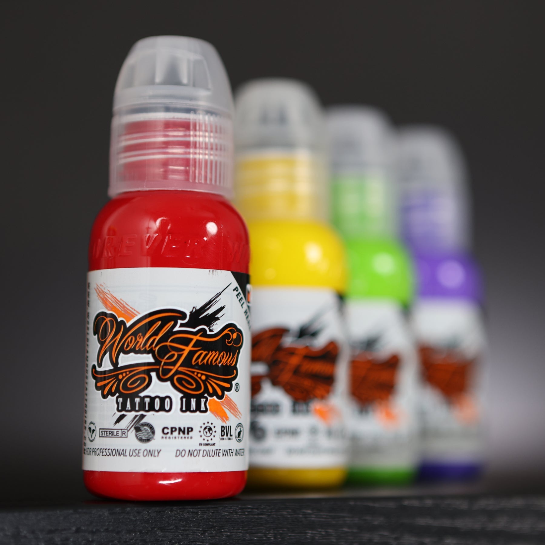 A bright red bottle of World Famous Tattoo Ink in sharp focus among a colorful lineup.