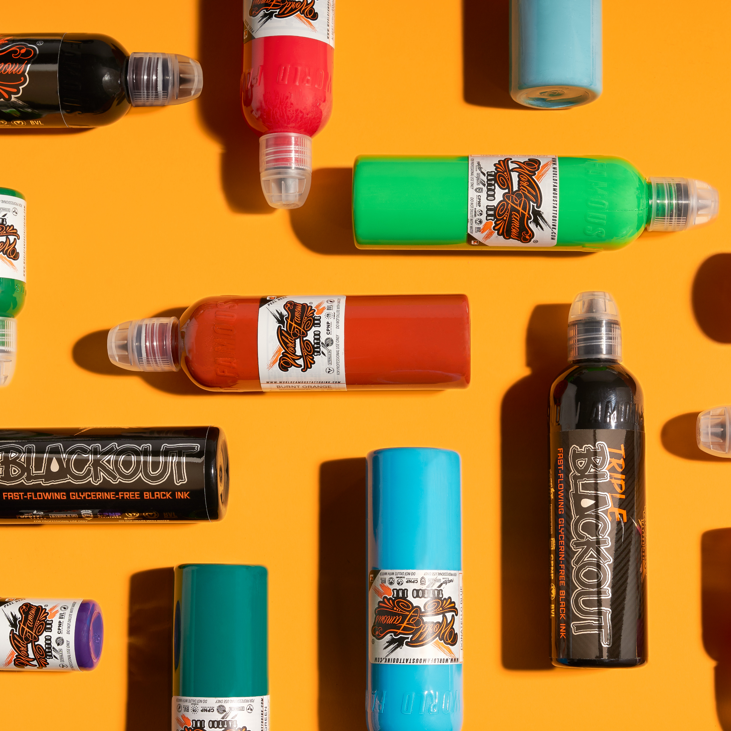 An overhead view of vibrant World Famous Tattoo Ink bottles scattered across a bright orange surface.